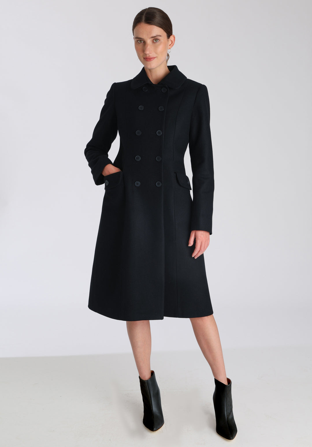 Model wearing the Tori coat in black cashmere blend, a vintage-inspired style with a double-breasted front, gently flared skirt, and curved detailing on the collar, pockets, and back belt.