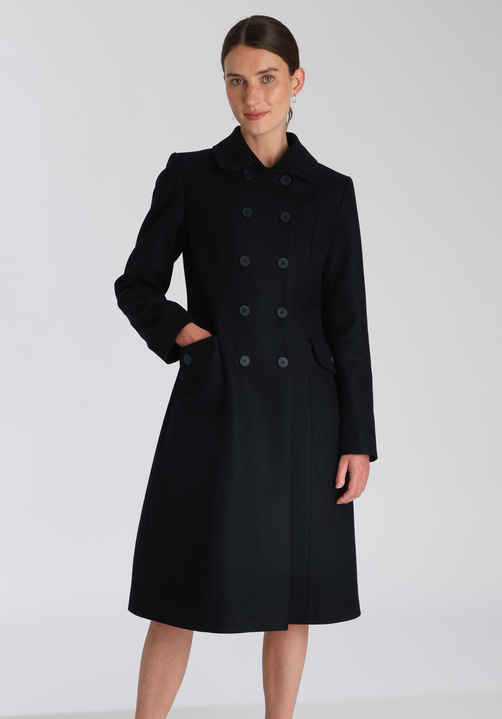 Model wearing the Tori coat in black cashmere blend, a vintage-inspired style with a double-breasted front, gently flared skirt, and curved detailing on the collar, pockets, and back belt.