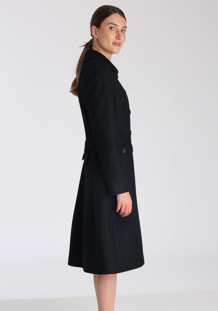 Model wearing the Tori coat in black cashmere blend, a vintage-inspired style with a double-breasted front, gently flared skirt, and curved detailing on the collar, pockets, and back belt.