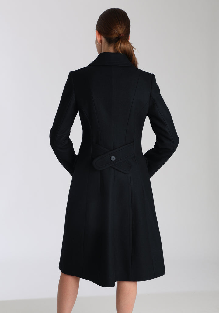 Model wearing the Tori coat in black cashmere blend, a vintage-inspired style with a double-breasted front, gently flared skirt, and curved detailing on the collar, pockets, and back belt.