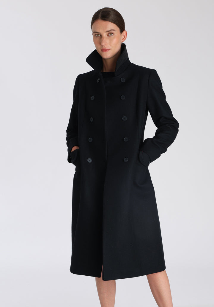 Model wearing the Tori coat in black cashmere blend, a vintage-inspired style with a double-breasted front, gently flared skirt, and curved detailing on the collar, pockets, and back belt.