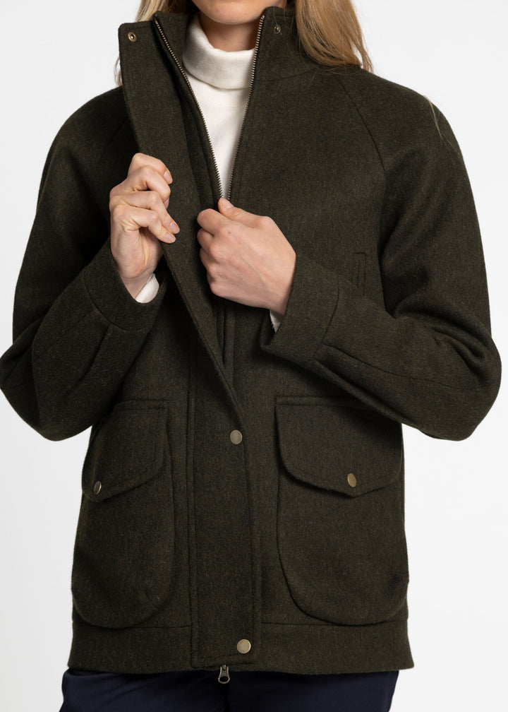 A close up of a woman zipping a dark green wool jacket with bronze clasp buttons.