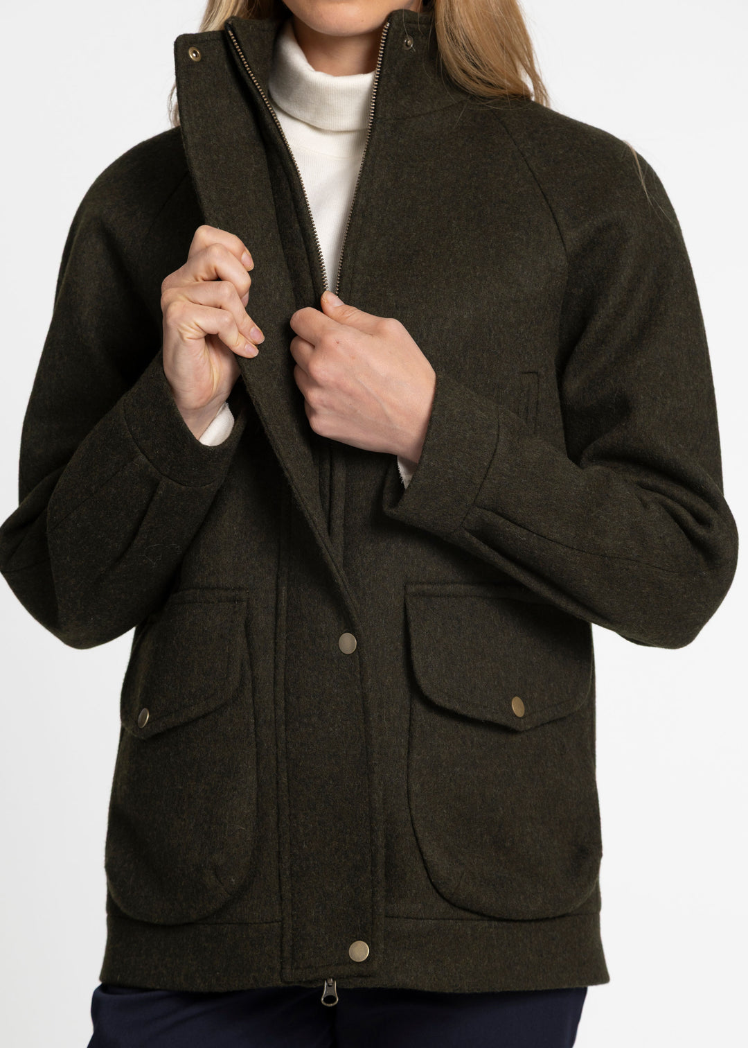 A close up of a woman zipping a dark green wool jacket with bronze clasp buttons.