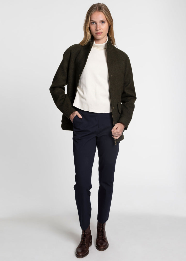 A woman modeling a dark green wool jacket paired with a white sweater and navy trousers.