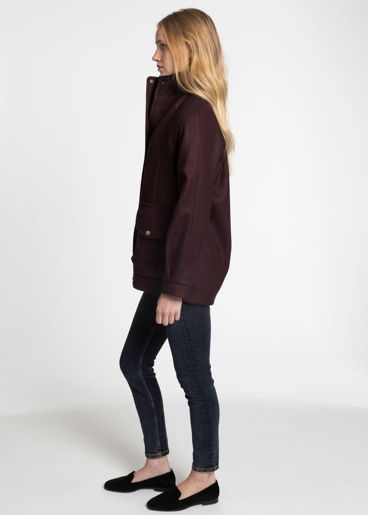 A side profile of a woman wearing a dark mulberry jacket. 
