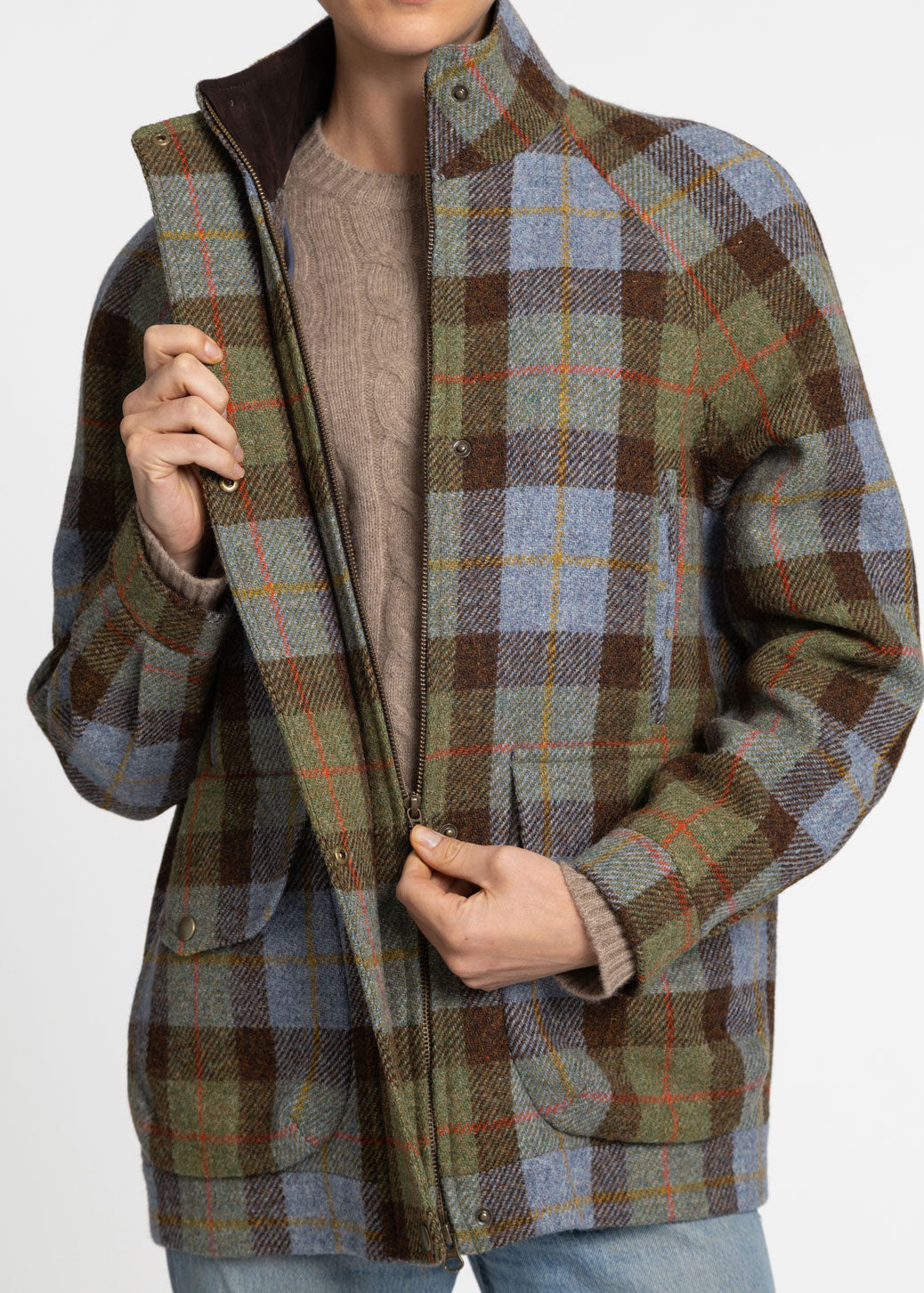 A person wearing a plaid jacket in muted blue, brown, olive green, and tan tones over a taupe sweater, shown against a plain light background.