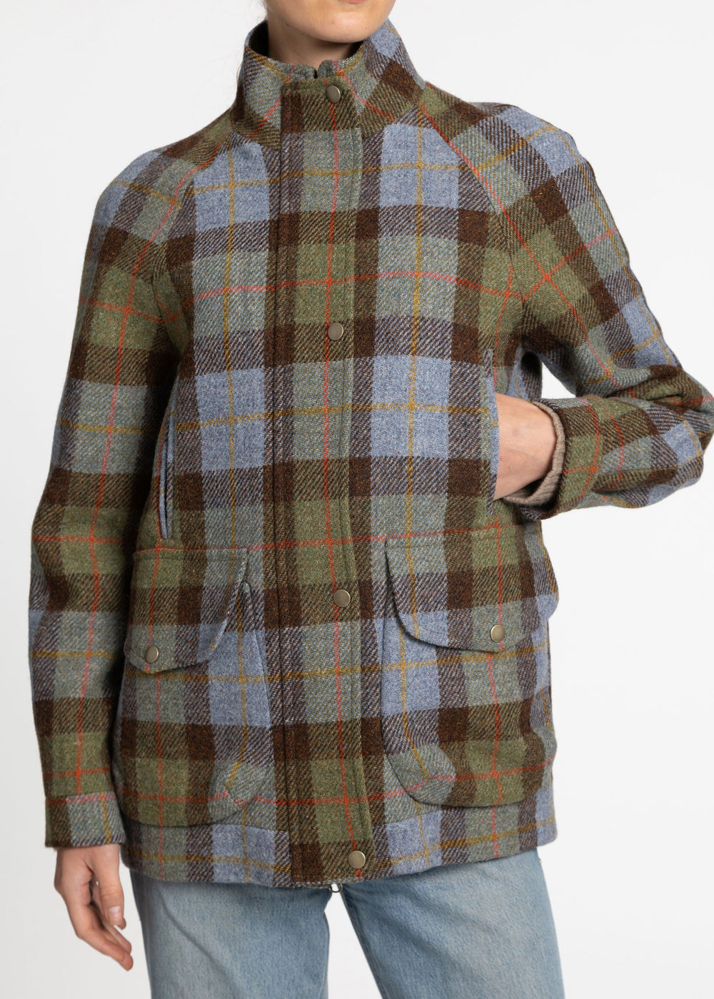A close up of a woman wearing a brown, blue and green plaid wool jacket with metal buttons. 