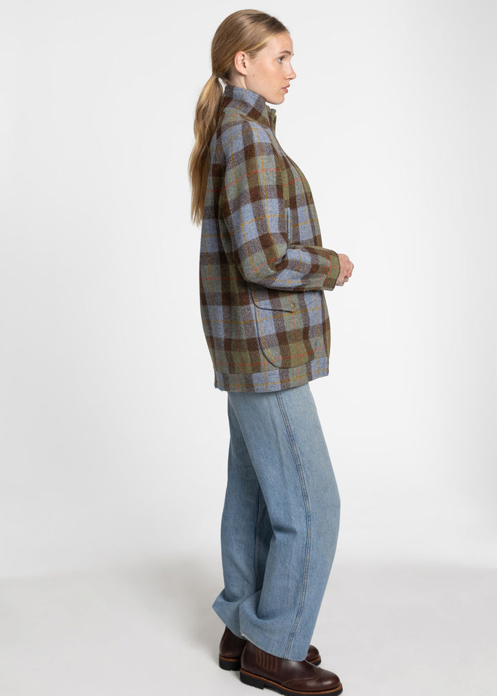 A side profile of a woman wearing a brown., blue and green plaid jacket paired with blue jeans and brown chelsea boots.