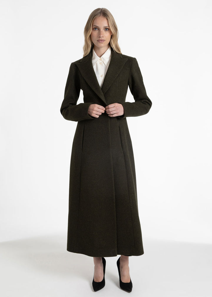 Woman wearing a tailored dark olive green wool coat with a white collared shirt underneath.