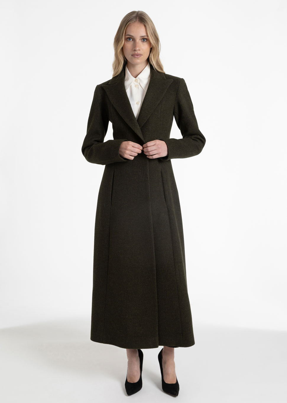 Woman wearing a tailored dark olive green wool coat with a white collared shirt underneath.