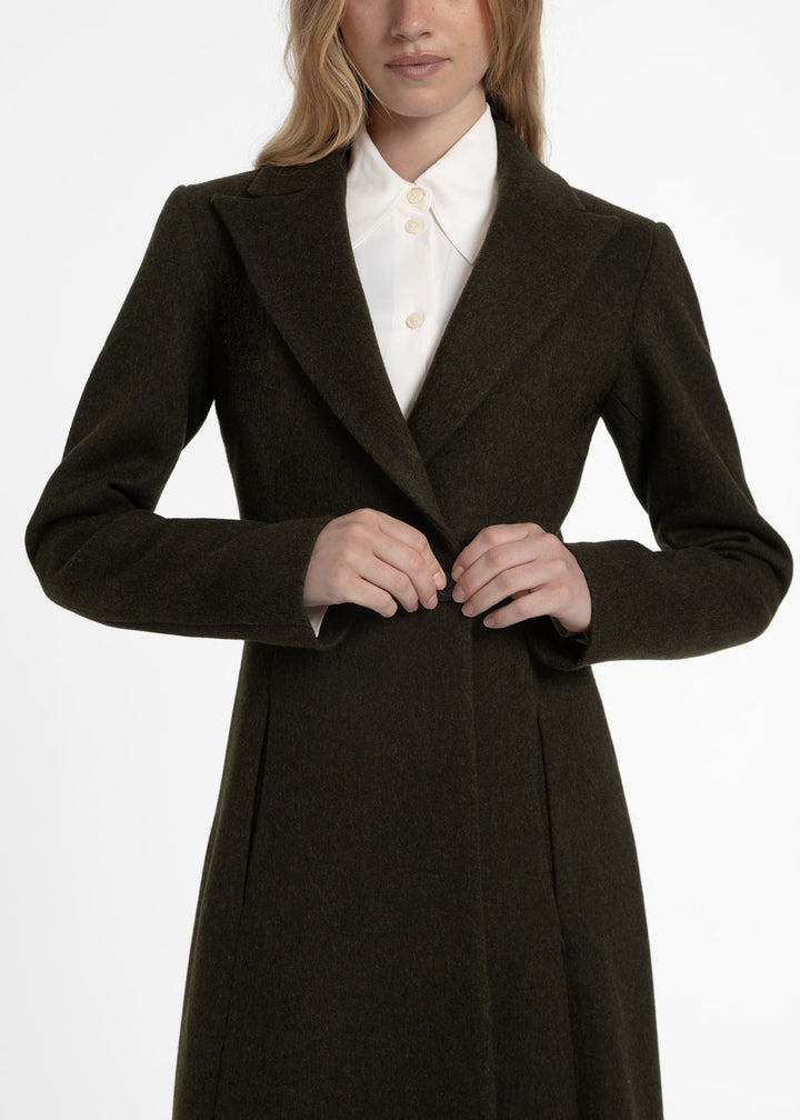 Close up of a woman wearing a dark olive green wool coat with a white collared shirt underneath.