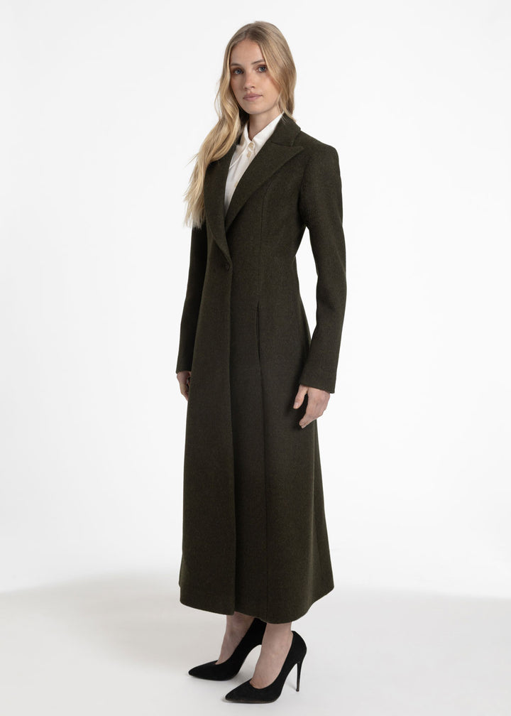 Side view of a woman wearing an olive green wool coat with a white collared shirt underneath.