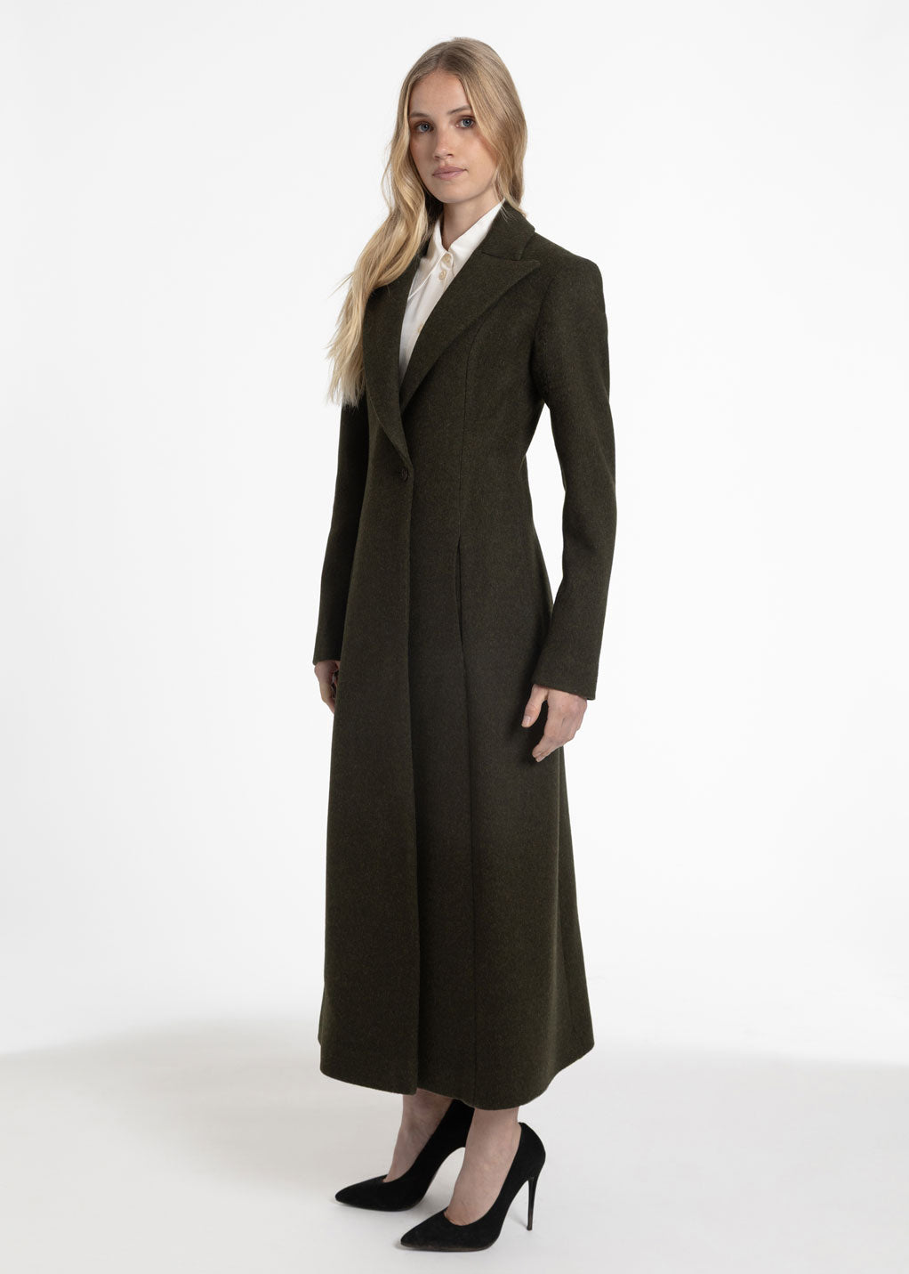 Side view of a woman wearing an olive green wool coat with a white collared shirt underneath.