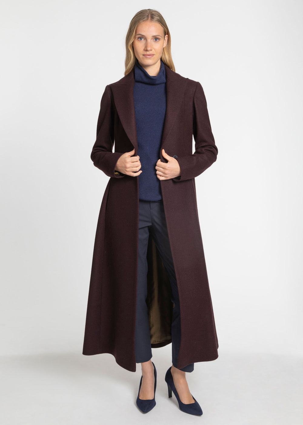 A woman wearing a mulberry wool coat over a navy turtleneck sweater and navy trousers.