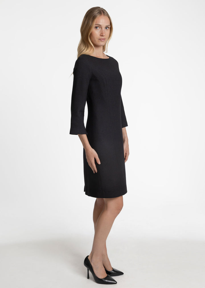 Side view of a model wearing a 3/4 length sleeve knee length black dress.