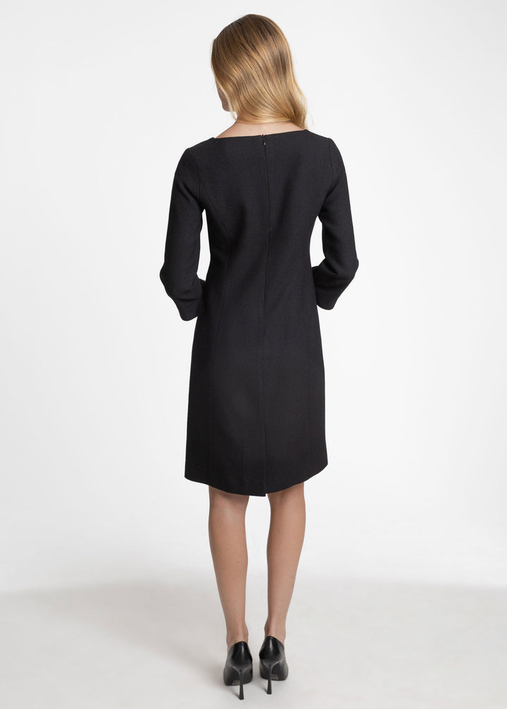 Back view of a woman wearing a black knee length sleeved dress with a back zip closure.