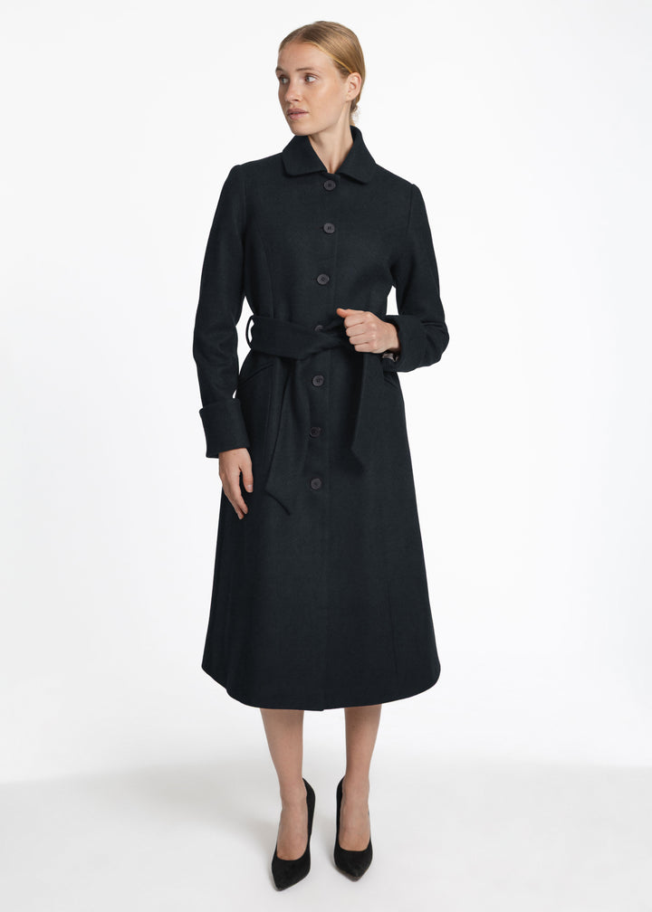A woman wearing a dark green wool coat with button and belted closure. 