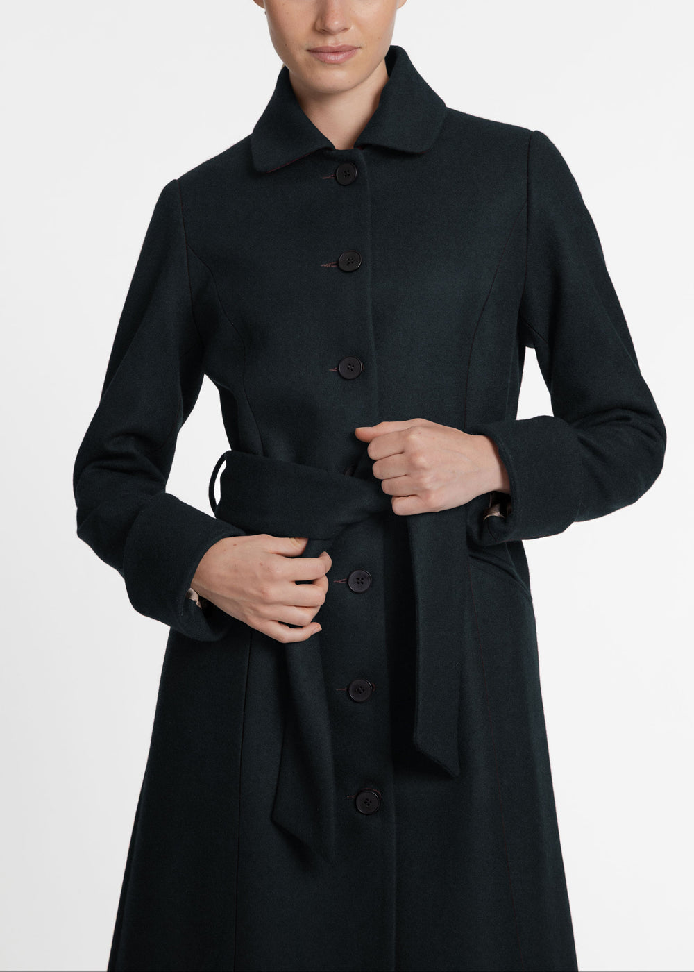 A close up of a woman wearing a dark green wool coat with a button front and belted closure.