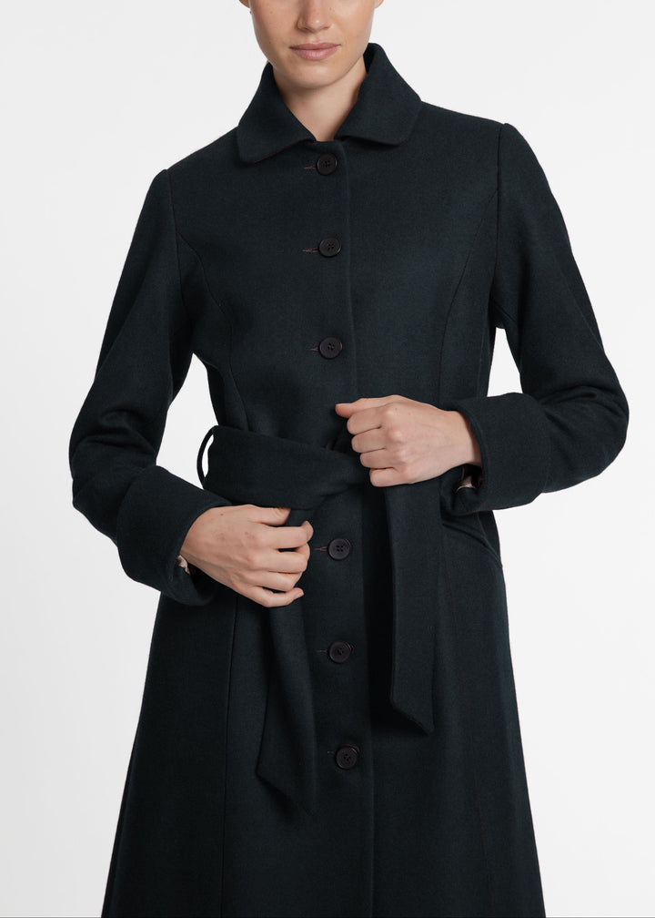 A close up of a woman wearing a dark green wool coat with a button front and belted closure.