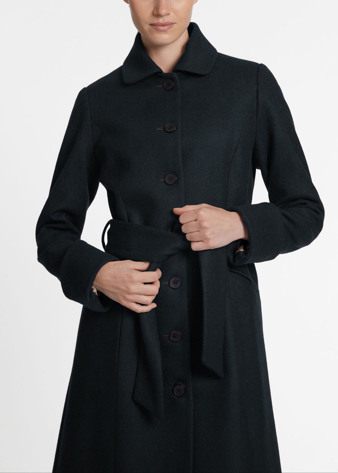 A close up of a woman wearing a dark green wool coat with a button front and belted closure.