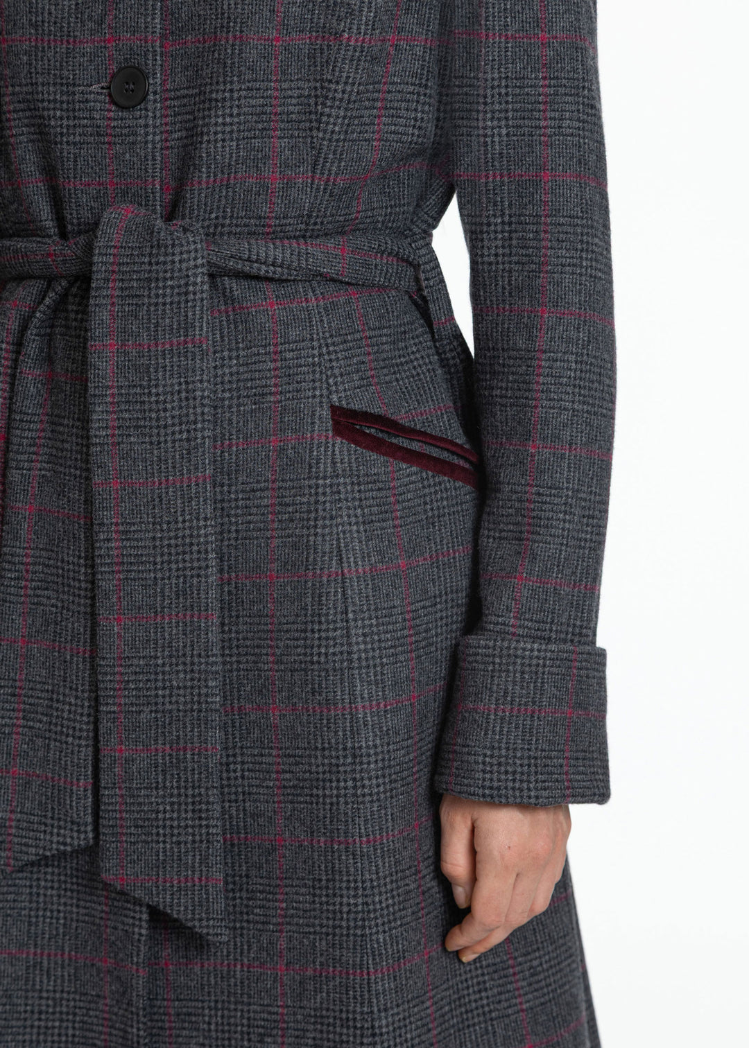 Close-up of a dark gray and black plaid coat with thin red windowpane lines, featuring a matching waist tie and a side pocket with a dark red lining.