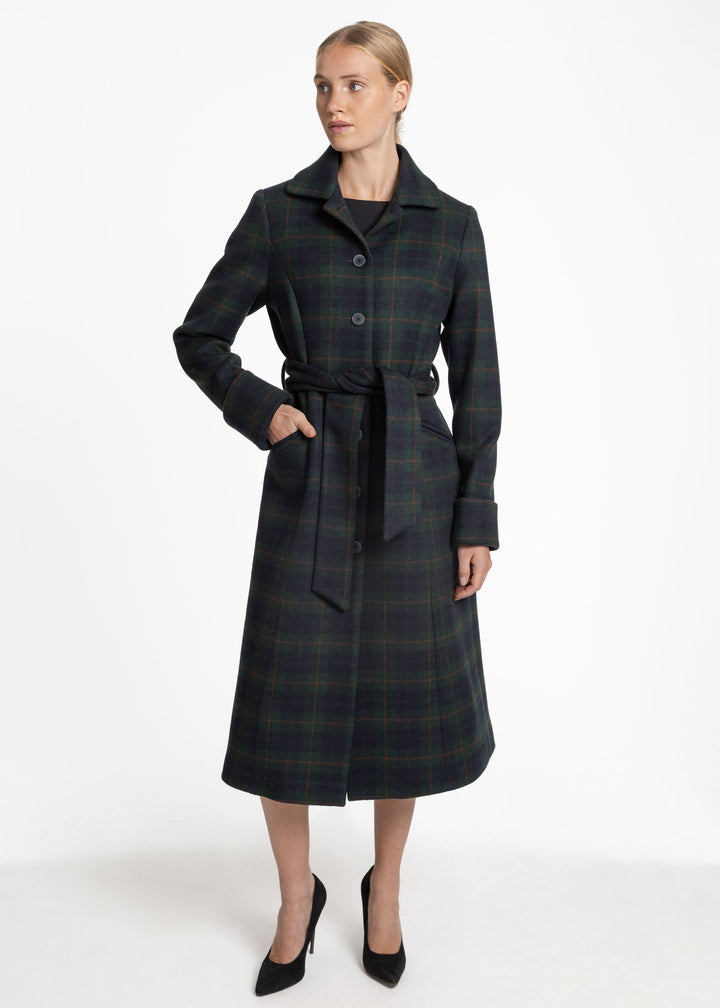 A woman modeling a dark green and black plaid wool coat with a matching waist tie belt, paired with black high heels, against a plain white studio background.