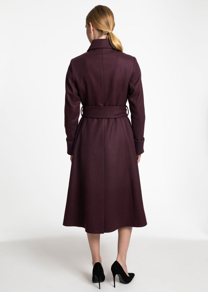 A woman viewed from the back wearing a knee-length dark plum coat with a matching waist tie and black high heels, against a plain white studio background.