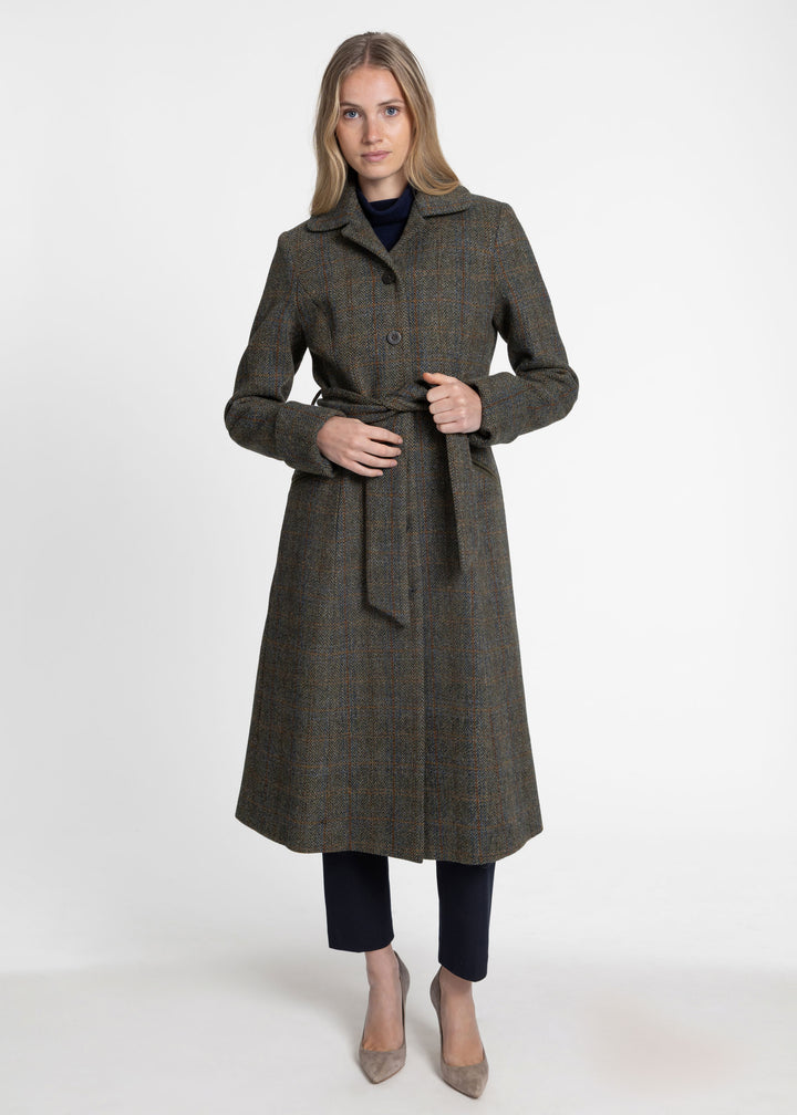 A woman modeling a long, plaid coat with a self-tie belt, worn over a dark top and paired with dark pants and beige heels, against a plain white studio background.
