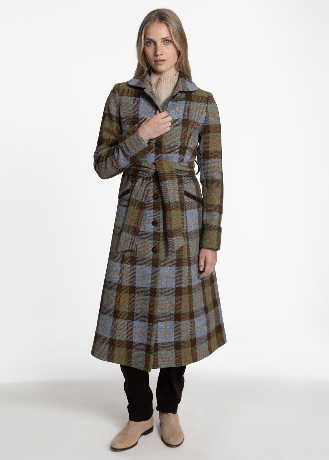 Woman wearing brown, blue and green plaid coat with a belt closure and brown buttons up the front.
