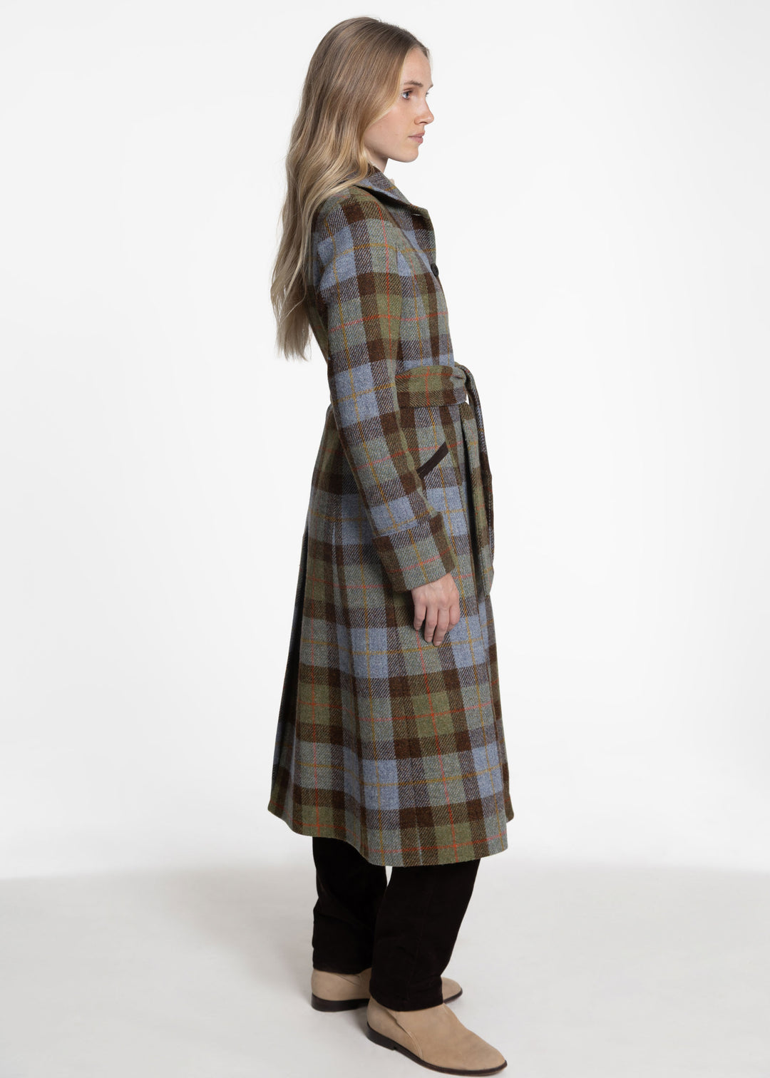 A side view of a woman wearing a belted plaid coat with blue, brown and green tones.