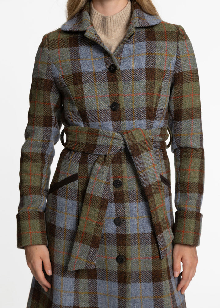 A woman wearing a belted plaid coat in muted green, brown, and blue-gray tones over a beige turtleneck, shown from the shoulders to the knees against a plain light background.