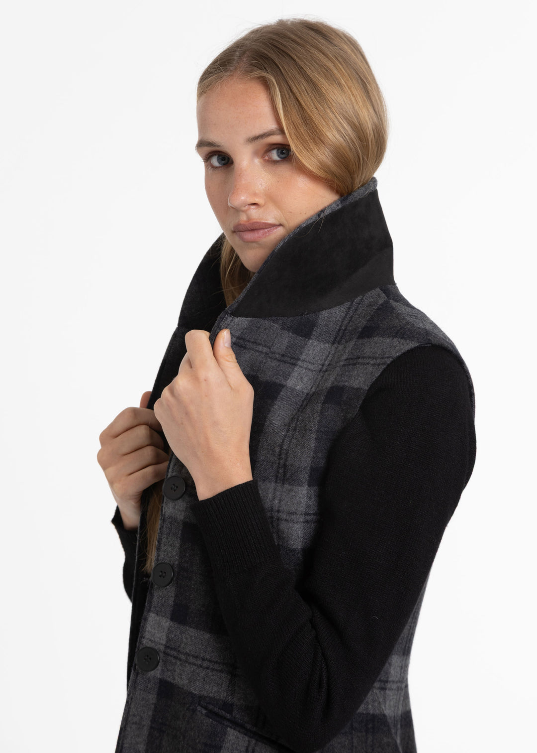 A woman wearing a black and gray plaid button-front waistcoat over a black long-sleeve top, photographed against a plain white studio background.