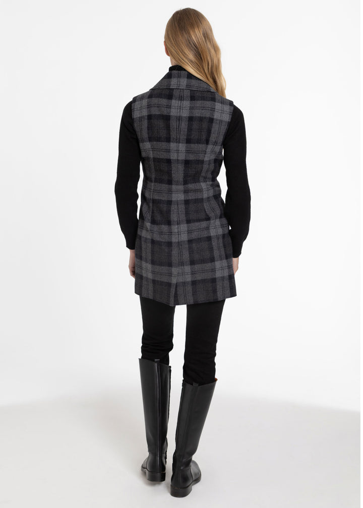 A woman shown from the back wearing a sleeveless black and gray plaid waistcoat over a black long-sleeve top, black pants, and black knee-high boots, against a plain white studio background.
