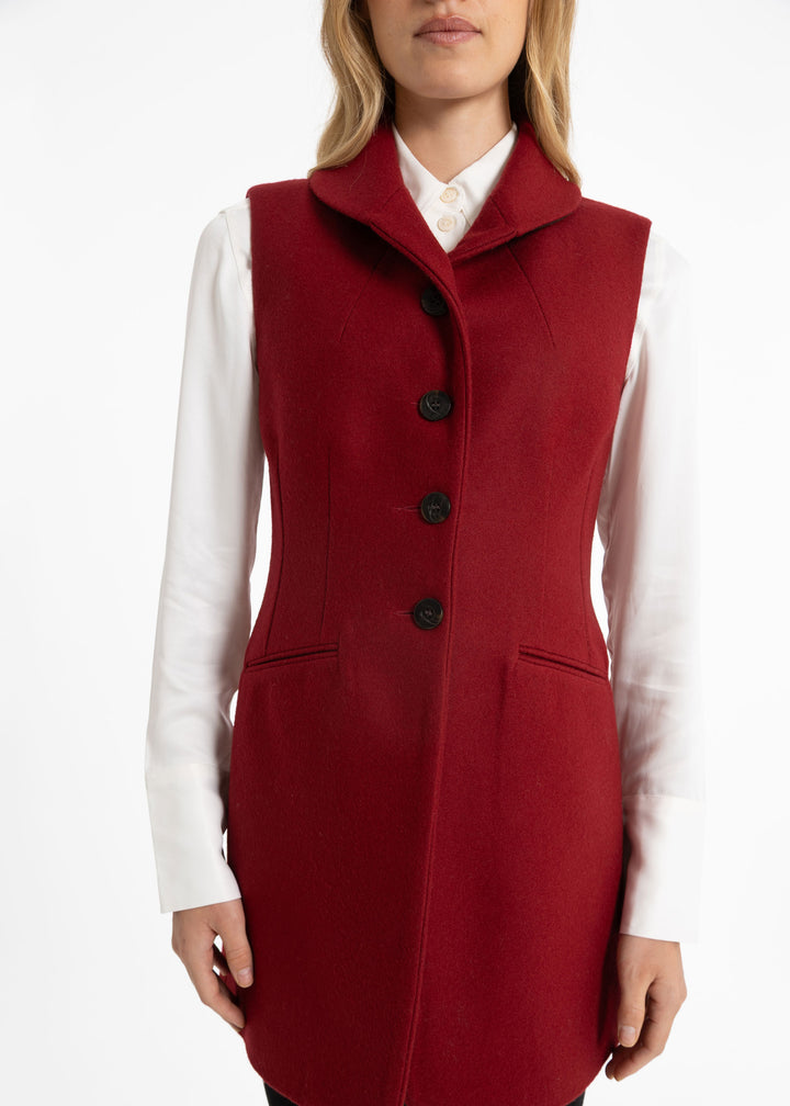 A woman wearing a sleeveless, structured red wool waistcoat over a white collared shirt, shown from the neck down against a plain white studio background.