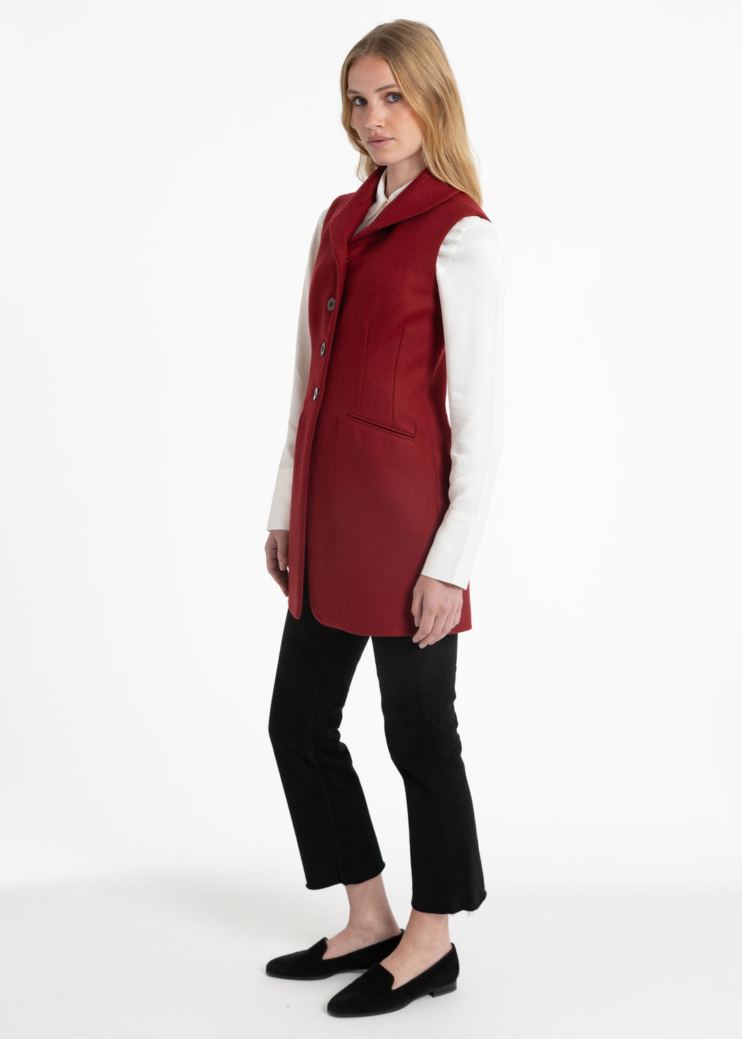 Side view of a woman wearing a red wool waistcoat with a white collared shirt underneath.