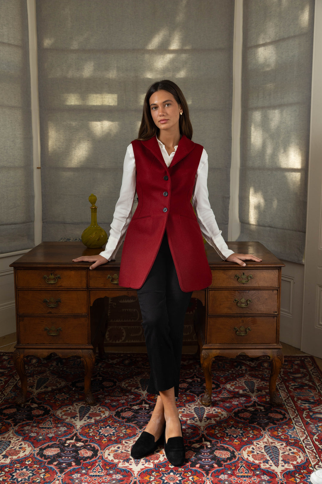 Woman wearing a red waistcoat with a desk in the backround.