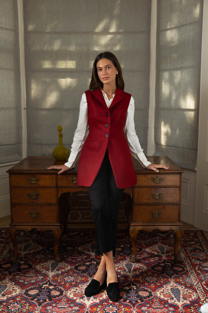Woman wearing a red waistcoat with a desk in the backround.
