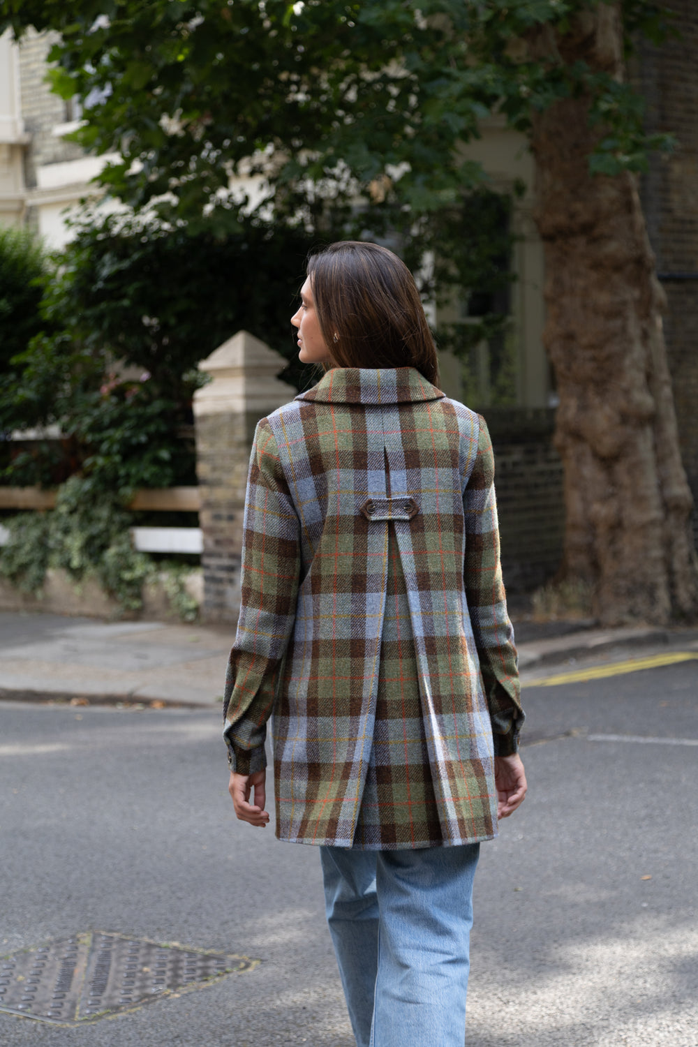 Back of a woman with a blue, brown and green plaid coat with a black pleating detail.