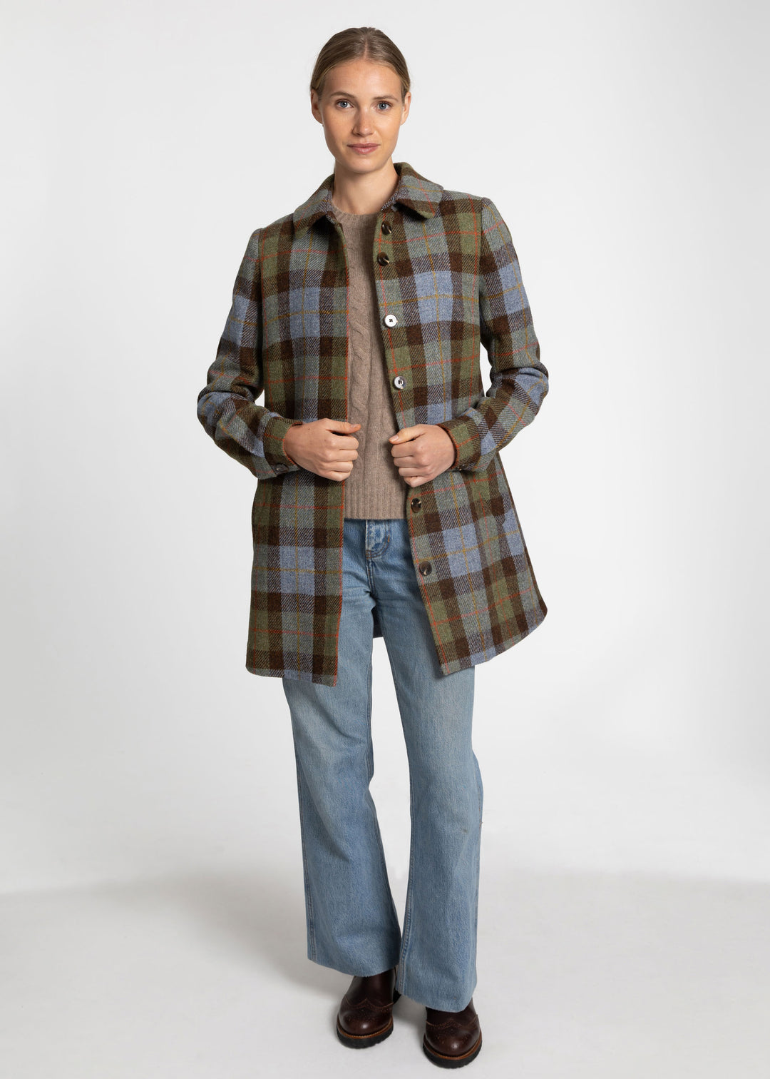 Woman wearing a brown, blue and green check plaid coat worn open with a beige sweater and blue jeans.