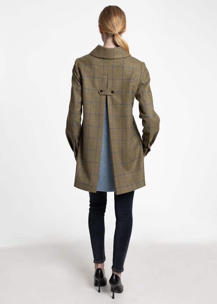 A woman shown from the back wearing a green and blue windowpane plaid coat with light blue peakaboo detail, paired with black skinny jeans and black heels, against a plain white studio background.