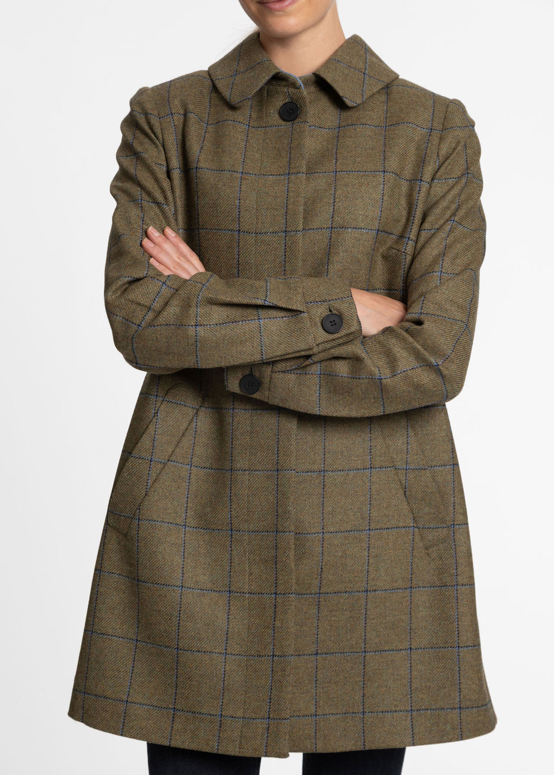 A woman wearing a green windowpane plaid coat with blue lines, standing with arms crossed against a plain white background.
