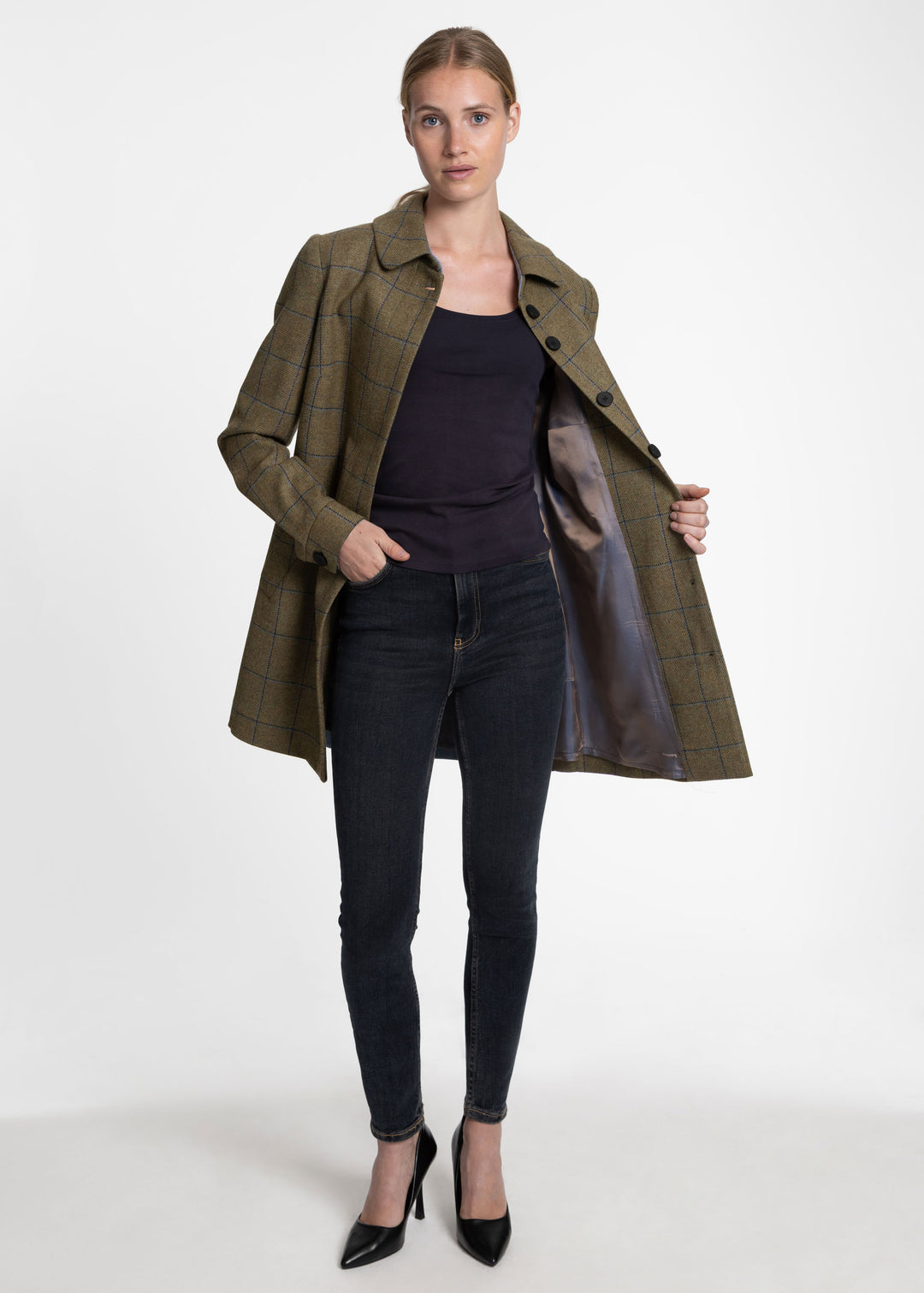A woman models a mid-length olive green plaid coat with a blue satin-lined interior, worn open over a dark top and black skinny jeans.