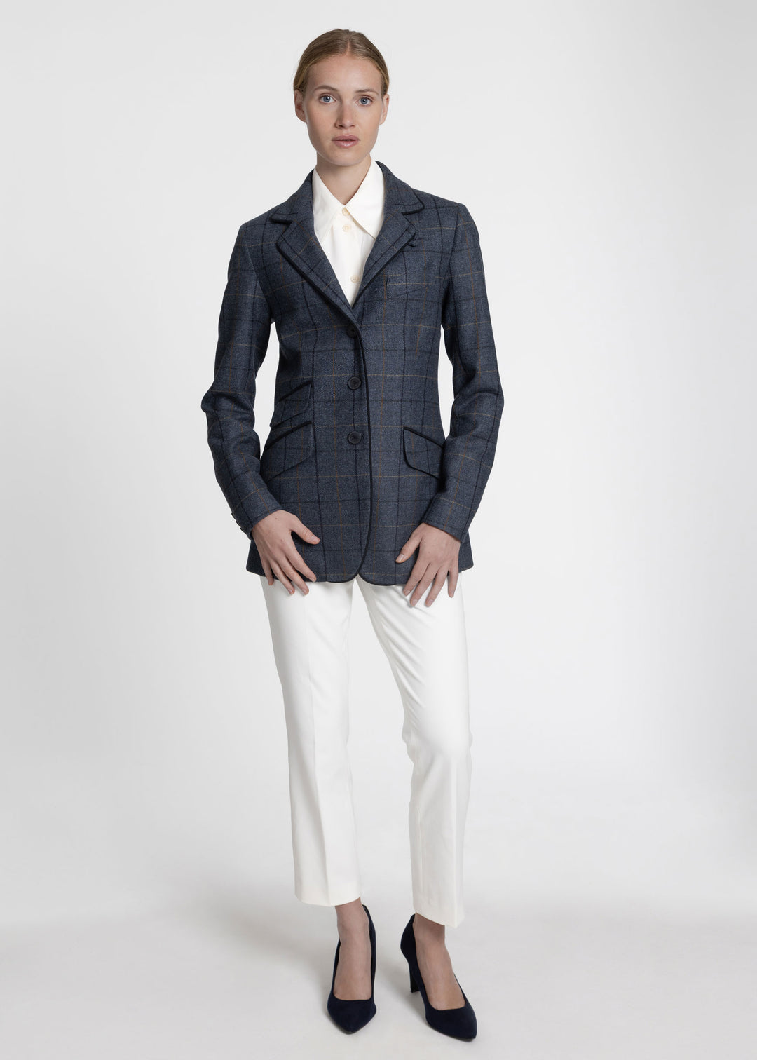 Woman wearing a blue jacket with orange and black windowpane check. Styled over a white collared shirt and white trousers. 