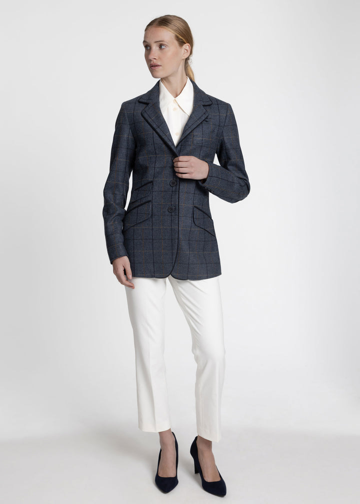 Woman wearing a navy jacket with black and orange windowpane check. Styled over a white collared shirt and white trousers.