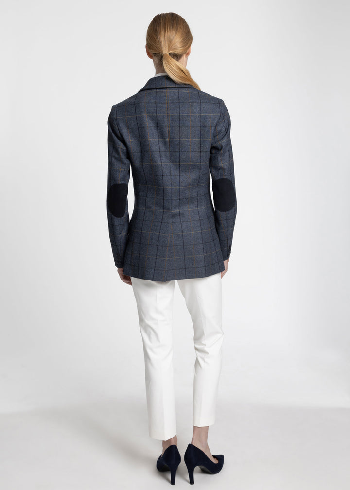 Back view of a woman wearing a navy jacket with black and orange windowpane check and navy elbow patches. Paired with white trousers and black heels.