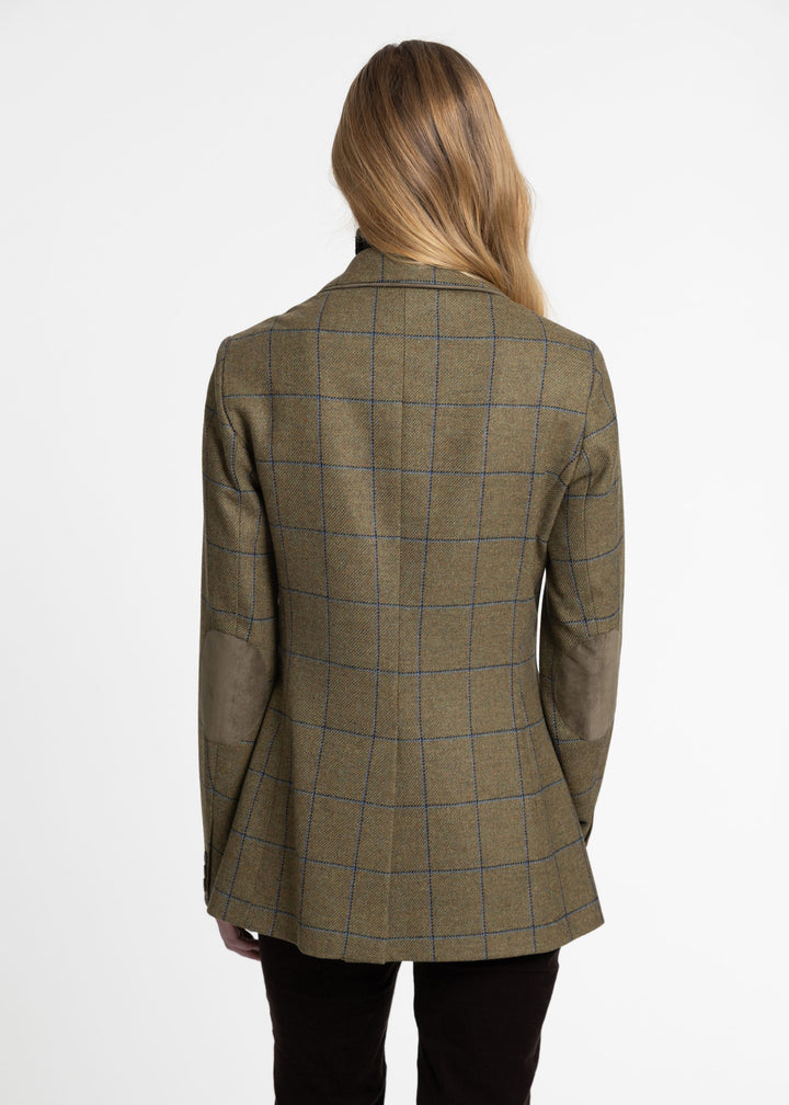 A woman viewed from the back wearing a tailored jacket in olive green with a blue windowpane plaid pattern and green suede elbow patches, paired with black trousers, against a plain white studio background.