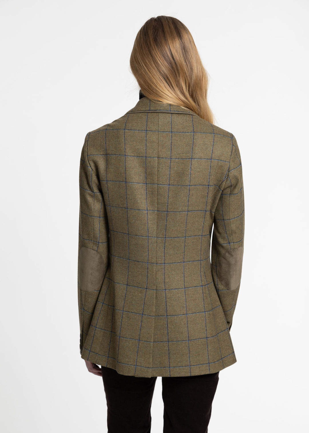 A woman viewed from the back wearing a tailored jacket in olive green with a blue windowpane plaid pattern and green suede elbow patches, paired with black trousers, against a plain white studio background.