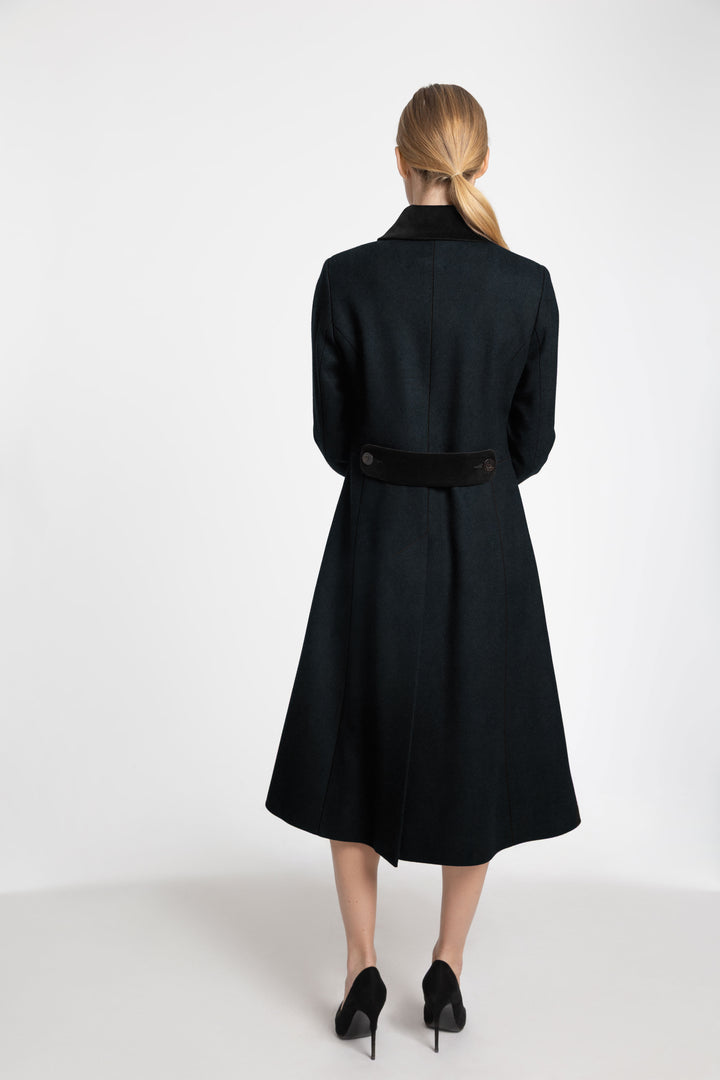 Back view of a woman wearing a dark green wool coat with black velvet collar, back belt and cuff detailing.