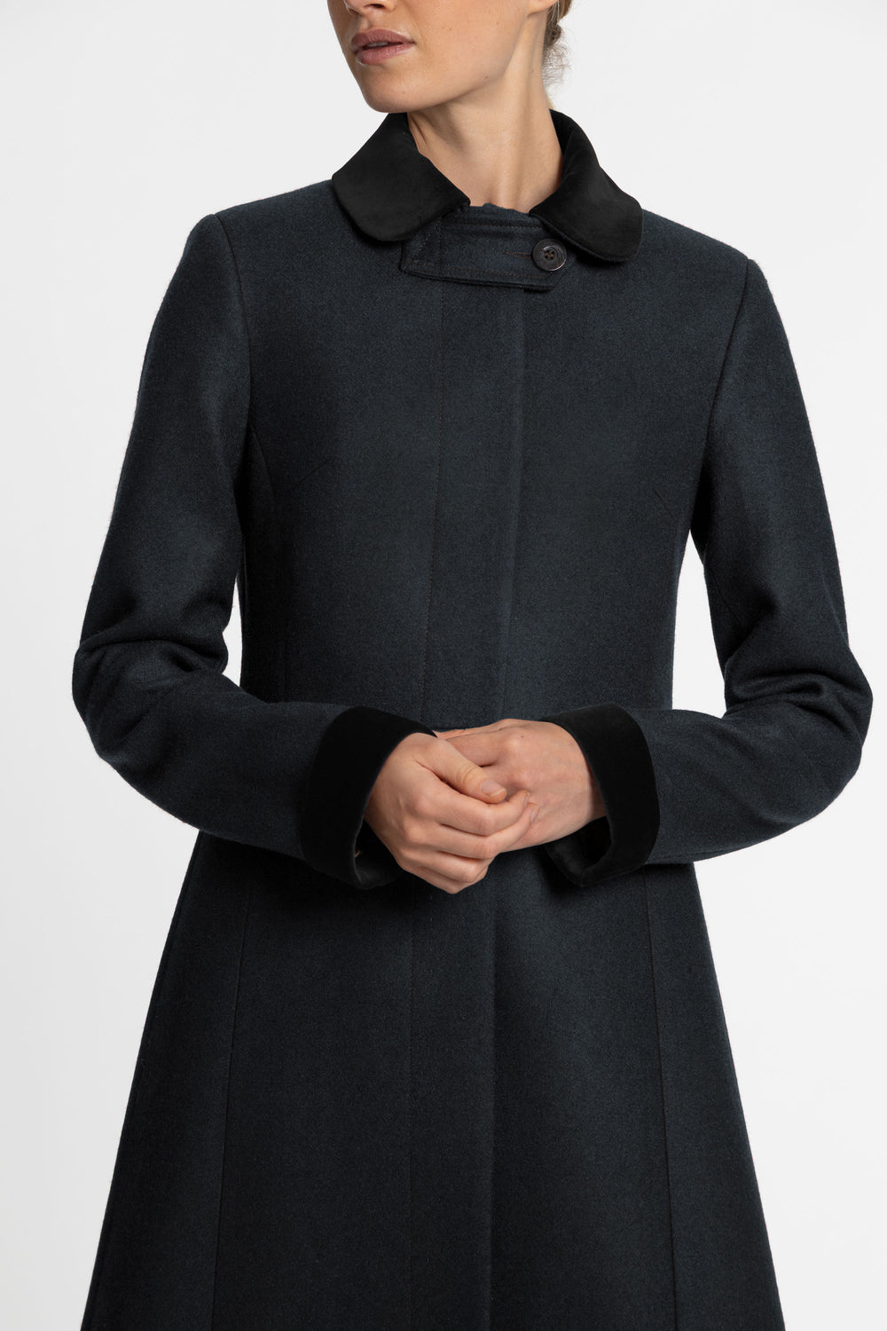 A close up of a woman wearing a dark green wool coat with black velvet collar and sleeve cuffs.