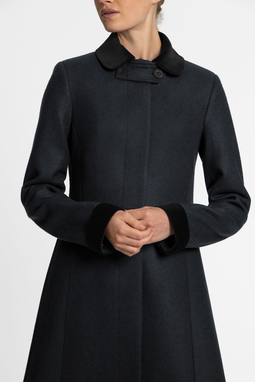 A close up of a woman wearing a dark green wool coat with black velvet collar and sleeve cuffs.